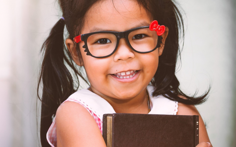 Little girl with pigtails and glasses holding a book